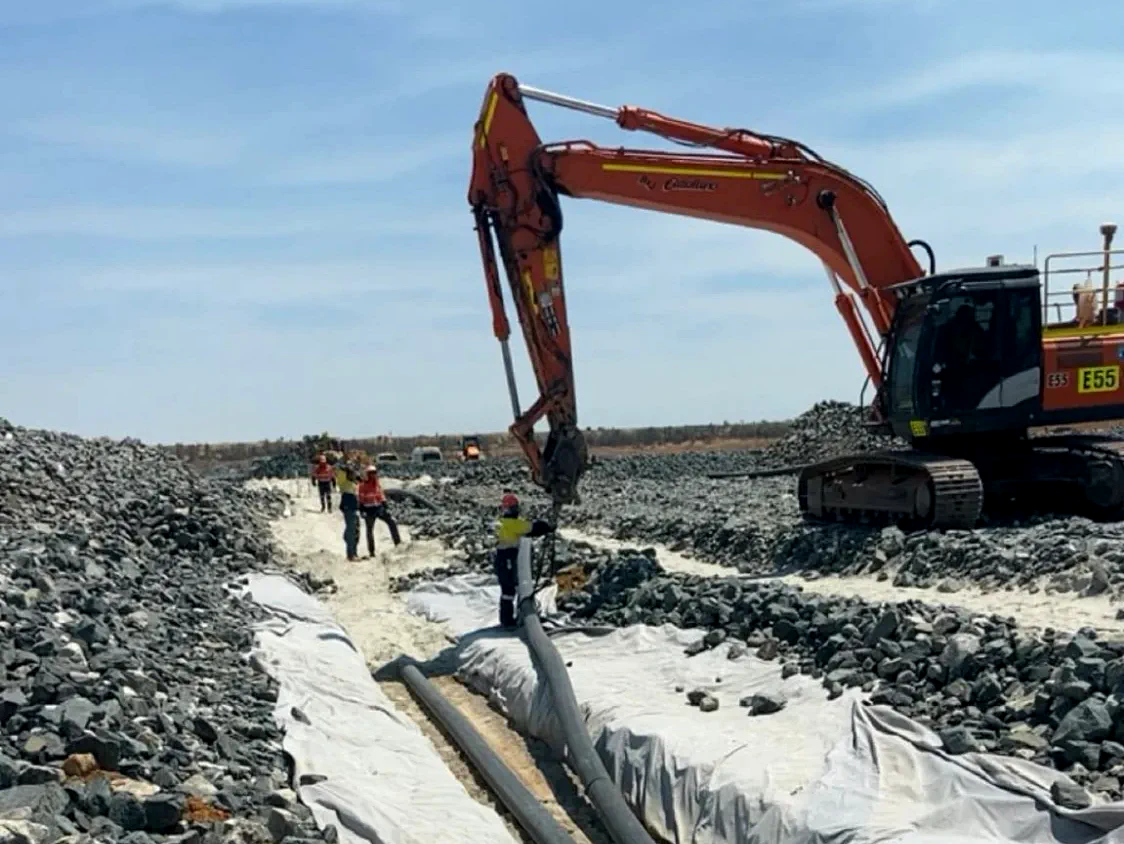 Geotextile-lined rock drain with slotted pipe being placed to spec