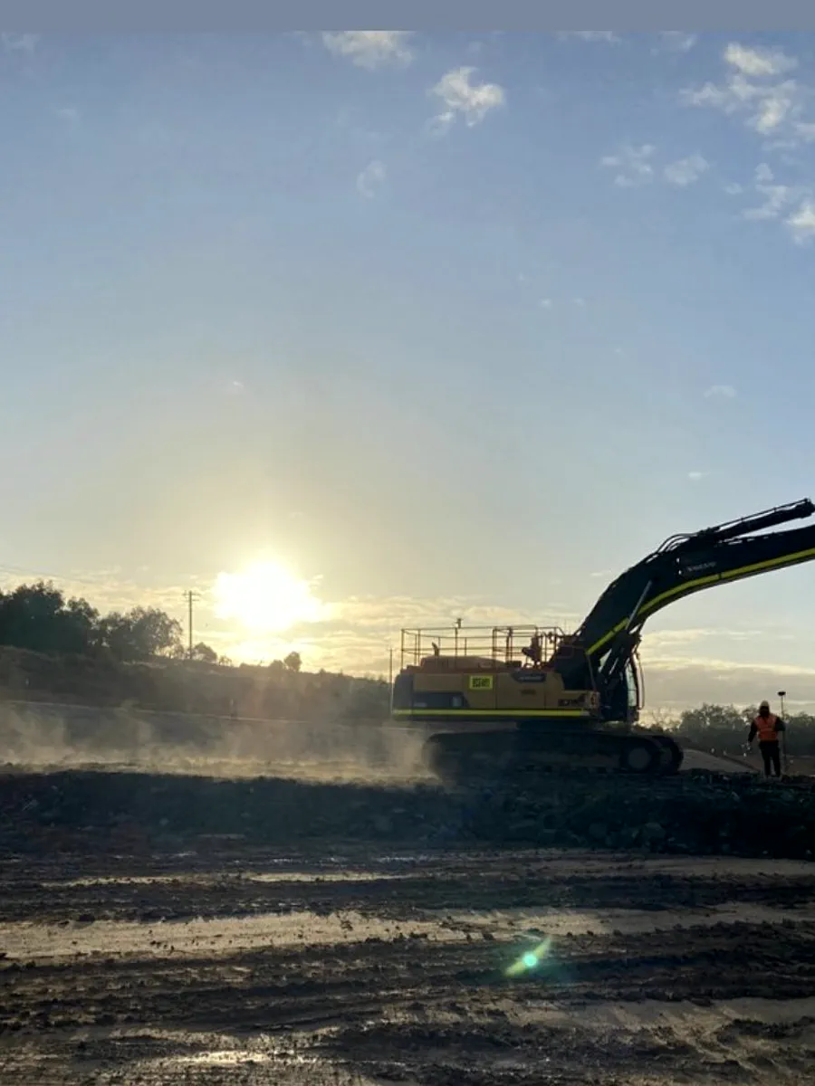 Excavator silhouetted at sunrise on a bulk earthworks pad