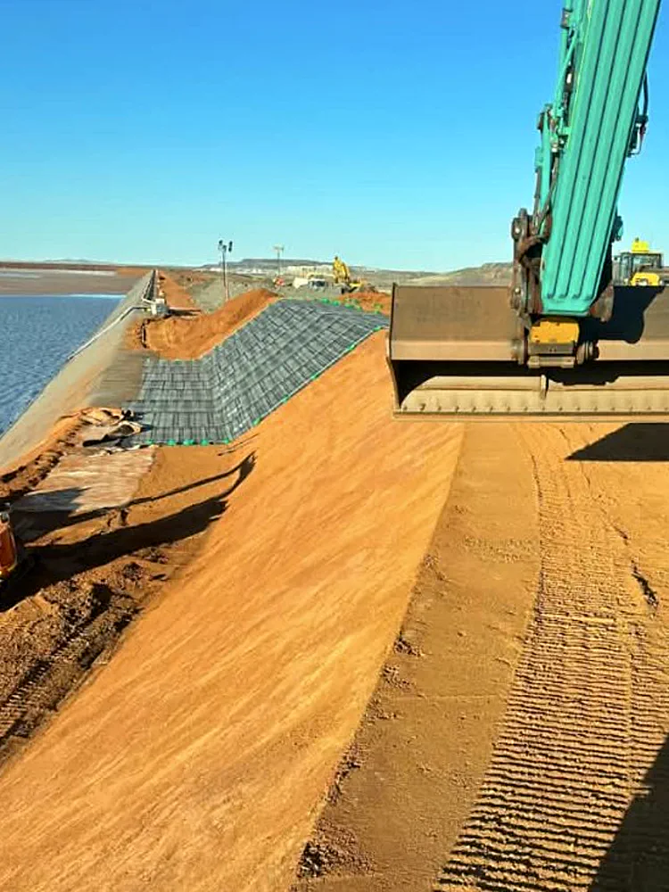Excavator placing fill over a geofabric-lined batter