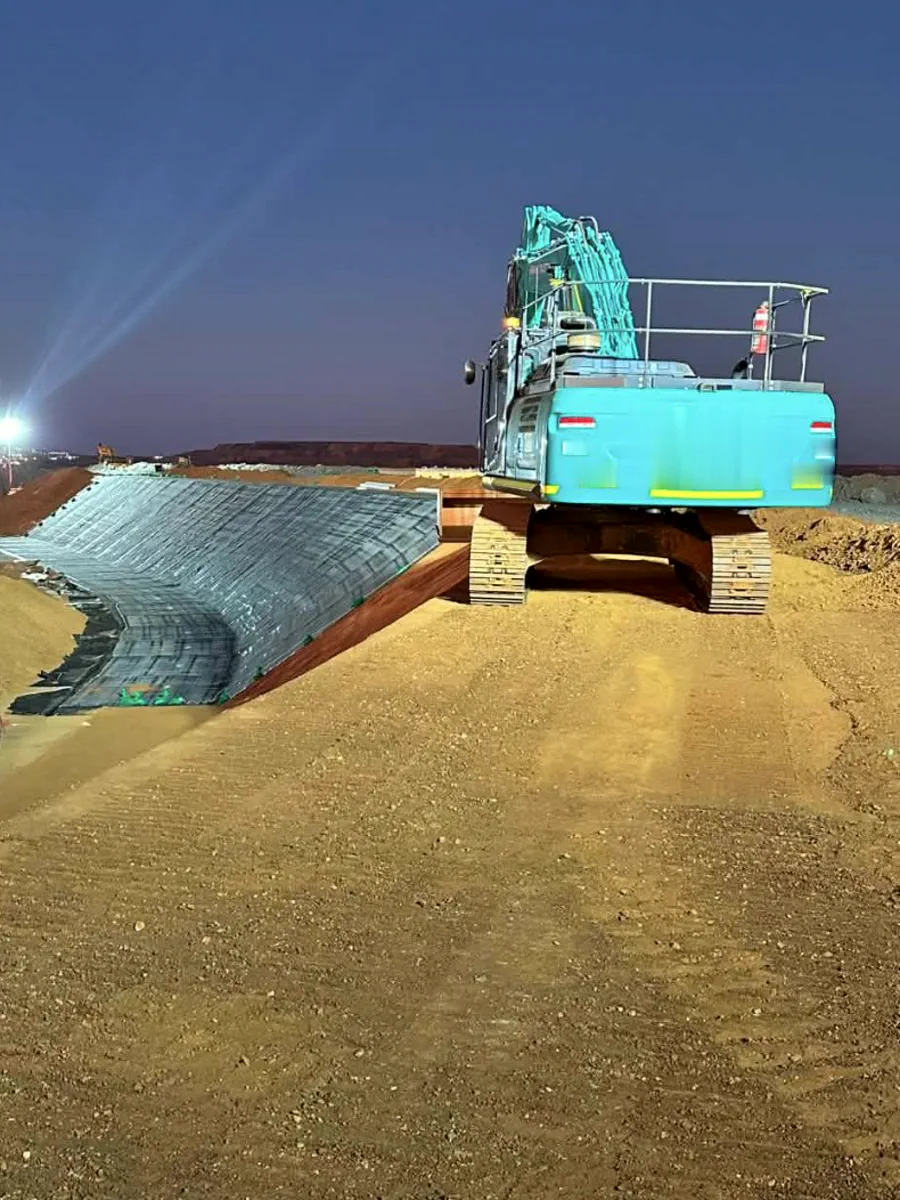 Excavator working a lined drainage batter under lights at night